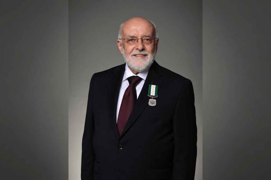 A photo of Dean LaBute in dark blazer and maroon tie, with the Queen's medal on his left lapel.