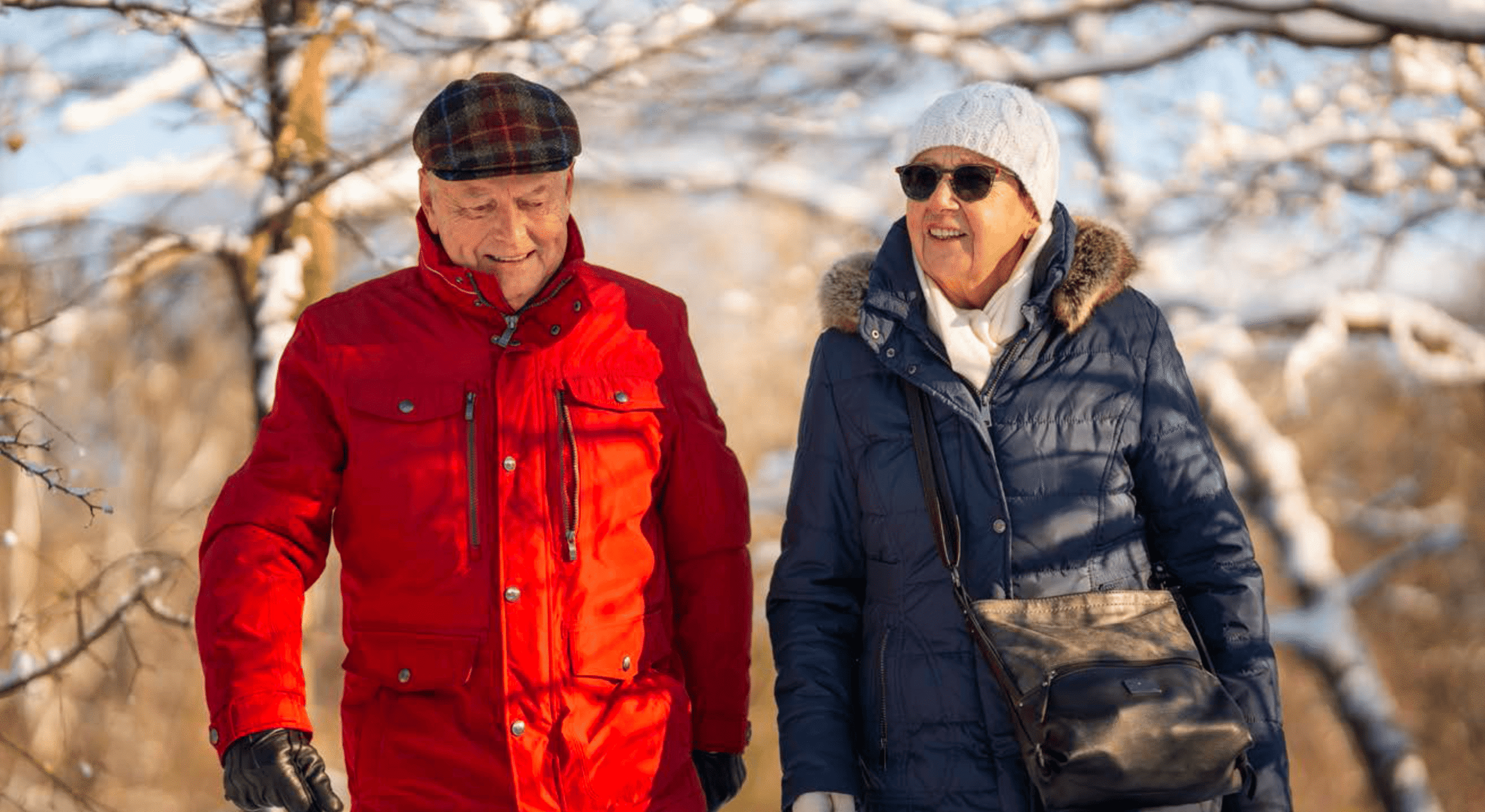 Two older adults enjoying a walk together on a snowy trail.